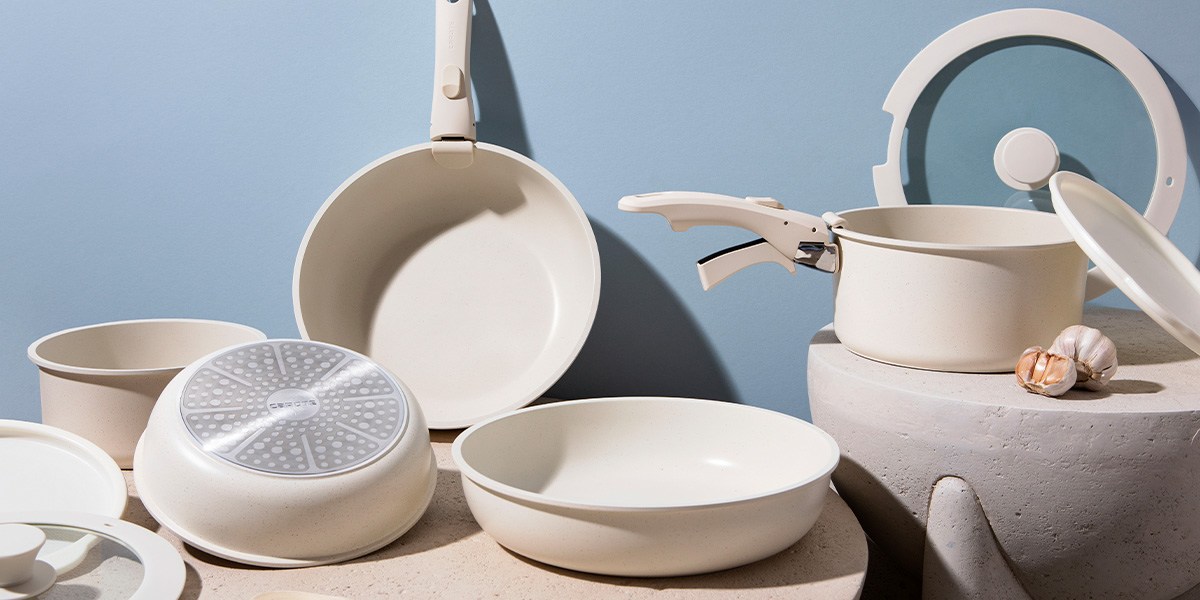 Carote 11-Piece Nonstick Pots and Pans Set stacked on glass table in front of product box