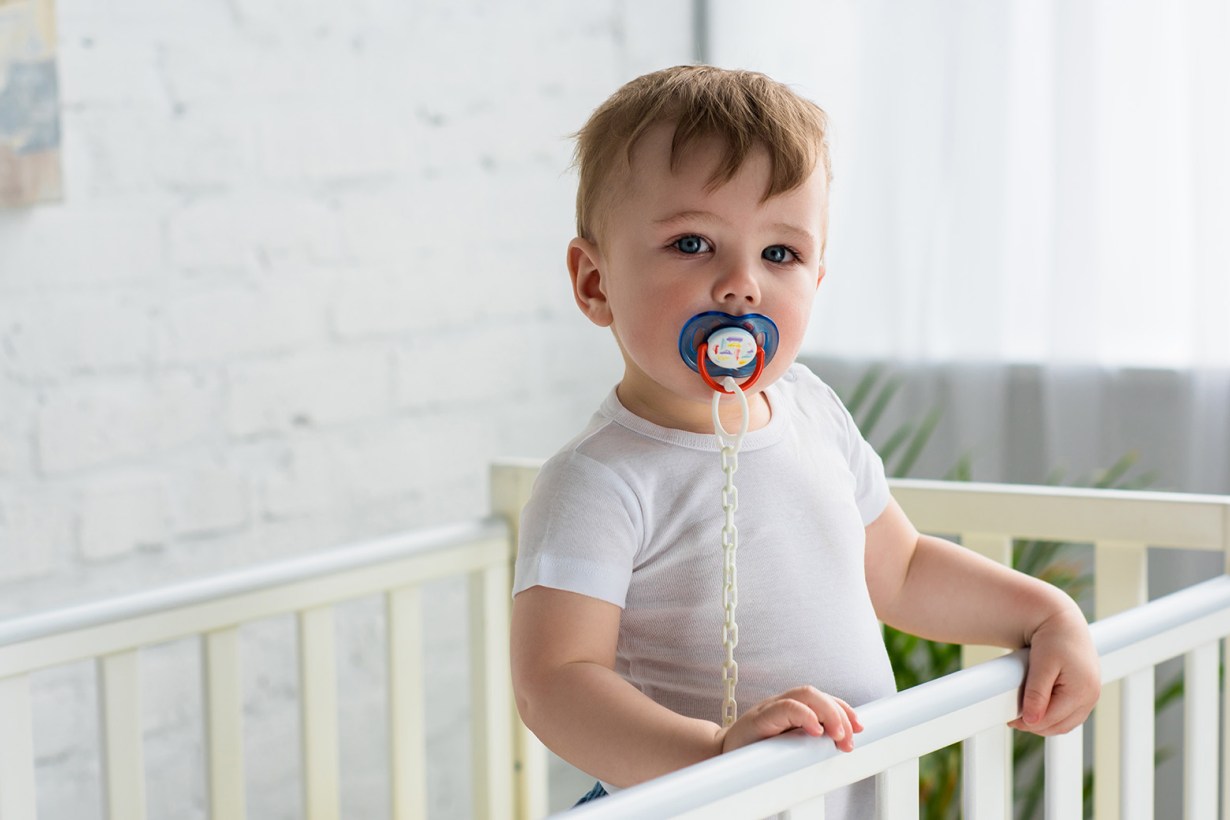 a child standing inside a crib with a pacifier